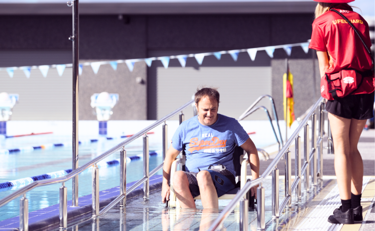 Lifeguard helping a patron with a disability down a pool ramp.