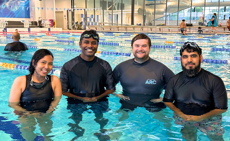 Three adult swimmers standing in the water next to a swim instructor.