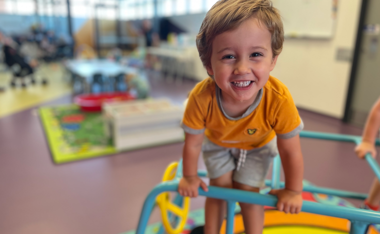 A boy climbing on play equipment, looking at the camera smiling.