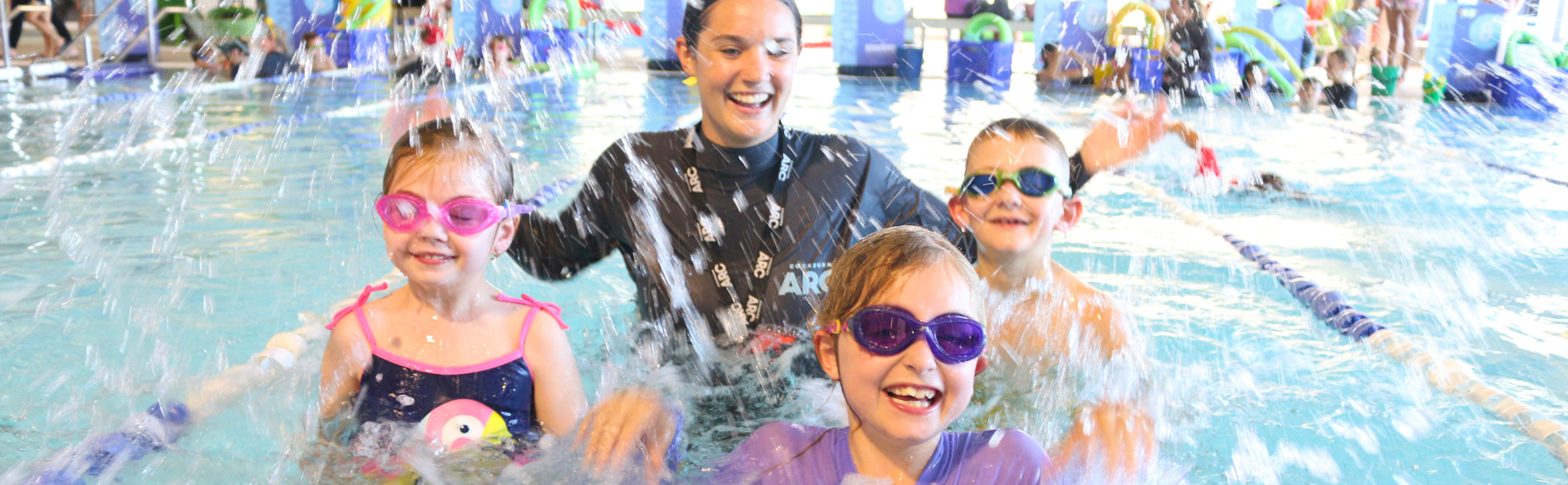 3 kids splashing in the water with an instructor.