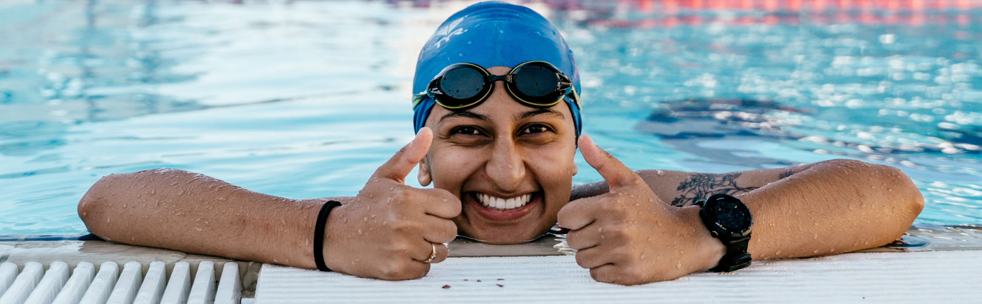 An adult swimmer with their thumbs up in the water.