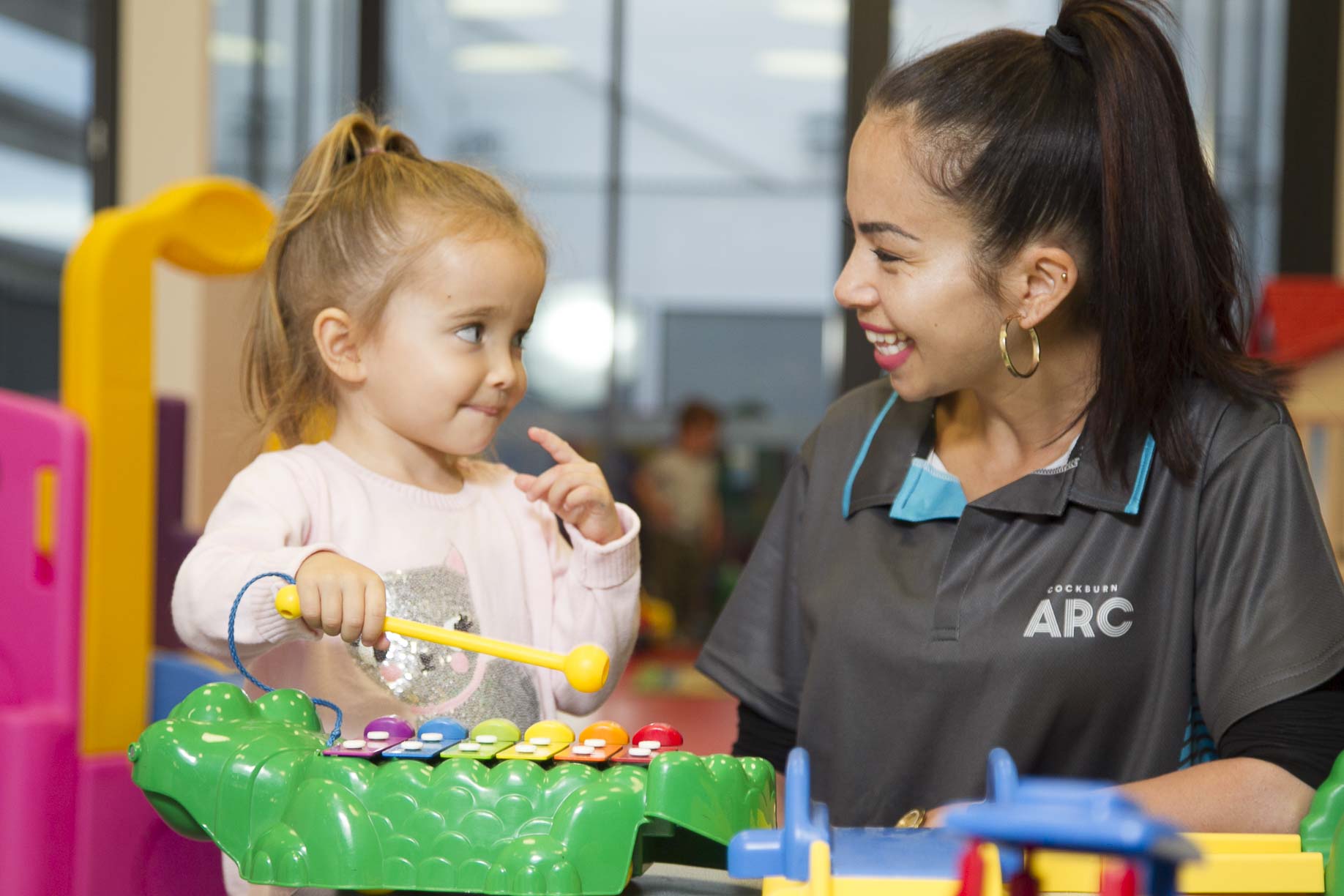 A creche attendant and child playing with an instrument.