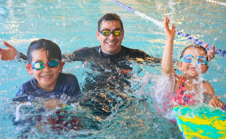 An instructor in the water splashing with two kids. 